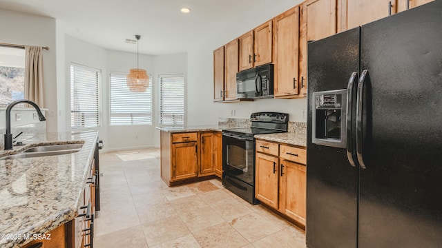 kitchen with hanging light fixtures, light stone countertops, black appliances, and a sink