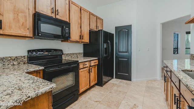 kitchen with black appliances, brown cabinetry, light tile patterned floors, baseboards, and light stone countertops