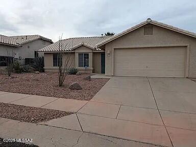 single story home with concrete driveway, an attached garage, a tile roof, and stucco siding