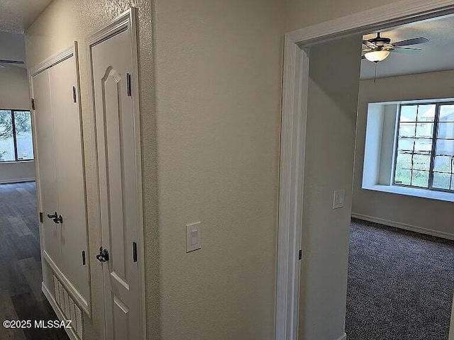 corridor featuring wood finished floors, baseboards, and a textured wall