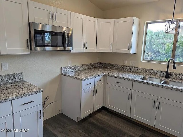 kitchen with a sink, stainless steel microwave, dark wood finished floors, and white cabinetry