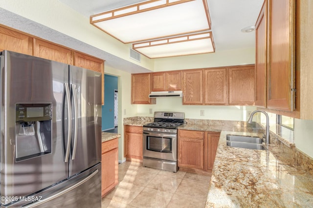 kitchen featuring visible vents, a sink, light stone counters, under cabinet range hood, and stainless steel appliances