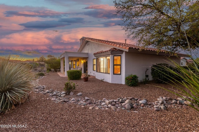 property exterior at dusk with stucco siding and a tiled roof