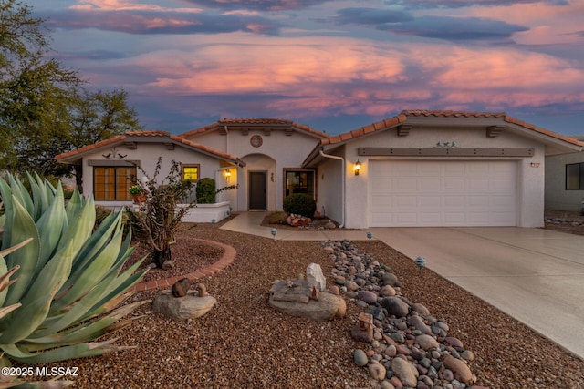 mediterranean / spanish-style house with a garage, stucco siding, driveway, and a tile roof