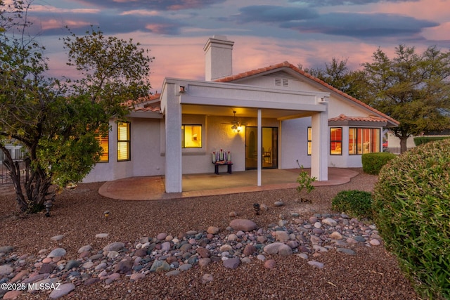 back of house with a tiled roof, a chimney, a patio area, and stucco siding