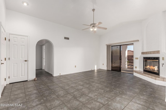 unfurnished living room featuring ceiling fan, arched walkways, high vaulted ceiling, a tile fireplace, and visible vents