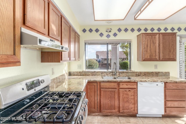 kitchen featuring white dishwasher, light stone countertops, gas stove, a sink, and under cabinet range hood