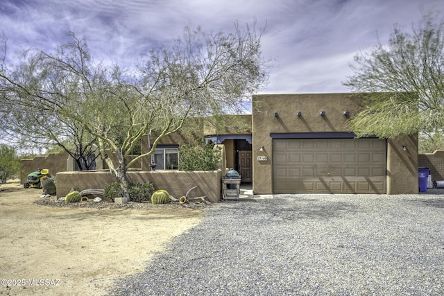 pueblo revival-style home featuring stucco siding, an attached garage, and driveway