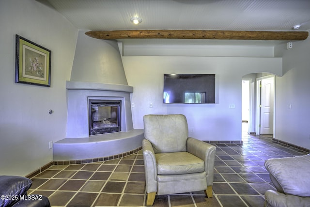 living area with tile patterned floors, beamed ceiling, arched walkways, a large fireplace, and baseboards