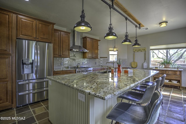 kitchen featuring visible vents, backsplash, stainless steel fridge, wall chimney exhaust hood, and light stone countertops