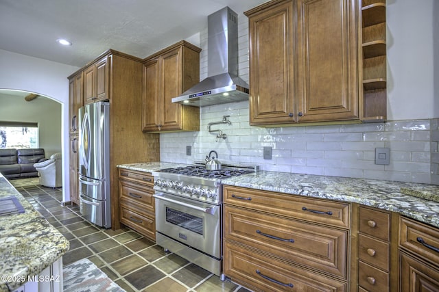 kitchen with light stone countertops, open shelves, arched walkways, appliances with stainless steel finishes, and wall chimney exhaust hood