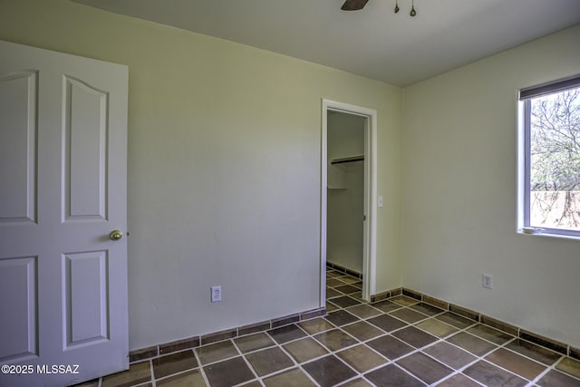 unfurnished bedroom with a closet, multiple windows, dark tile patterned flooring, and ceiling fan