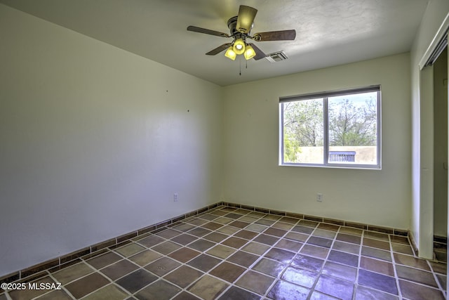 spare room with dark tile patterned flooring, a ceiling fan, and visible vents