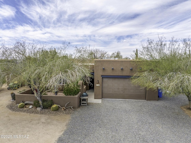 pueblo-style home with gravel driveway, an attached garage, and stucco siding