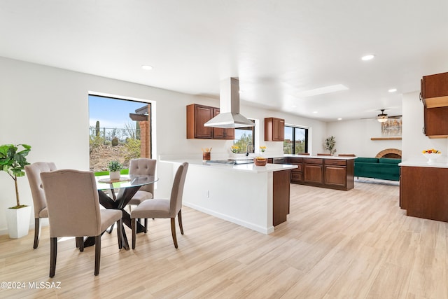 kitchen with a peninsula, a fireplace, island range hood, stainless steel stovetop, and light countertops