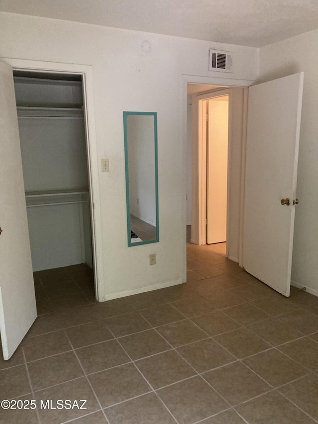 unfurnished bedroom featuring visible vents, dark tile patterned flooring, and a closet