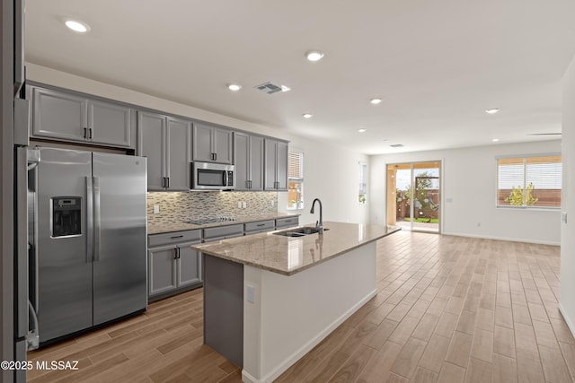 kitchen featuring visible vents, backsplash, gray cabinets, stainless steel appliances, and a sink