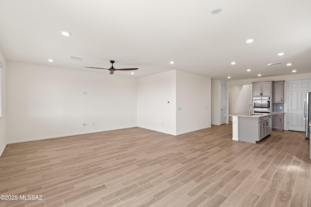 unfurnished living room featuring light wood-style floors, visible vents, and ceiling fan