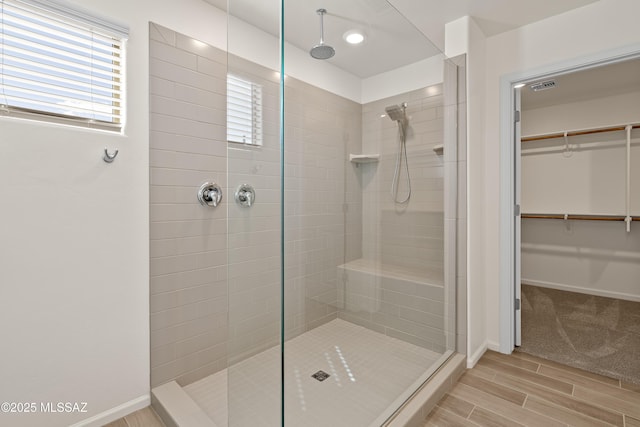 full bath with visible vents, a walk in closet, baseboards, wood finish floors, and a stall shower