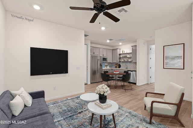 living room with light wood-type flooring, visible vents, baseboards, and ceiling fan