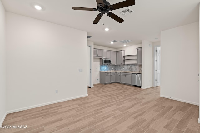 kitchen with a ceiling fan, light wood finished floors, gray cabinets, appliances with stainless steel finishes, and backsplash