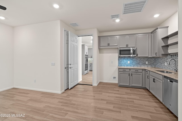 kitchen featuring visible vents, gray cabinets, a sink, open shelves, and appliances with stainless steel finishes