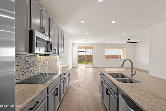 kitchen featuring backsplash, ceiling fan, appliances with stainless steel finishes, light wood-style floors, and a sink