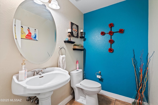 half bathroom with tile patterned flooring, toilet, baseboards, and a sink