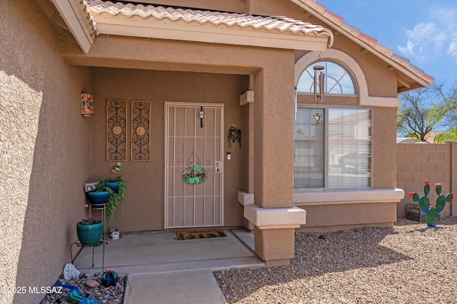 view of exterior entry with a tiled roof, stucco siding, and fence