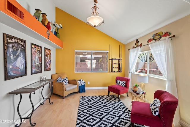 living area with lofted ceiling, wood finished floors, visible vents, and baseboards