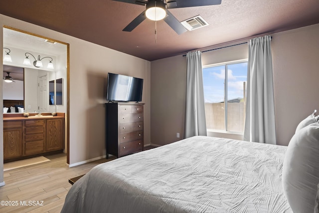bedroom featuring a sink, a textured ceiling, light wood-type flooring, baseboards, and visible vents