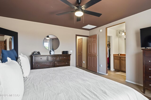 bedroom featuring baseboards, ensuite bath, wood finished floors, and a ceiling fan