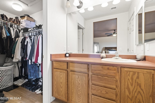 bathroom featuring visible vents, wood finished floors, vanity, a ceiling fan, and a walk in closet