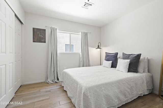 bedroom with baseboards, visible vents, a closet, and wood finished floors