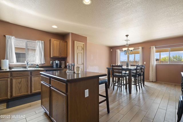 kitchen with a sink, a breakfast bar area, wood tiled floor, dark countertops, and an inviting chandelier
