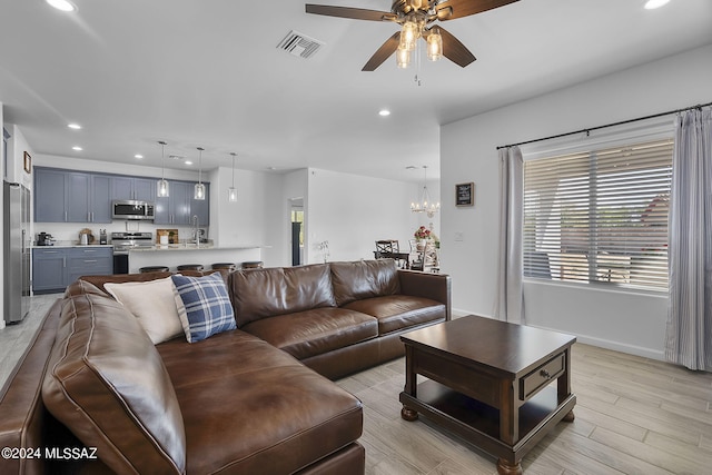 living area featuring visible vents, baseboards, recessed lighting, light wood-style floors, and ceiling fan with notable chandelier