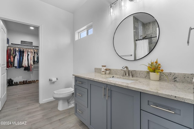 full bath featuring a spacious closet, baseboards, wood finish floors, toilet, and vanity