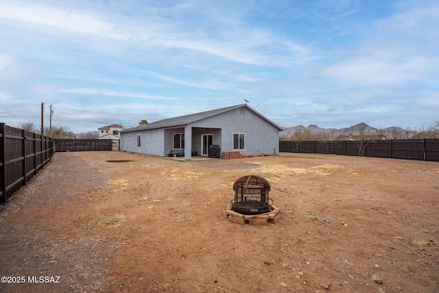 back of property with stucco siding, a fire pit, and a fenced backyard