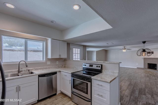 kitchen featuring a sink, open floor plan, stainless steel appliances, a peninsula, and light wood finished floors