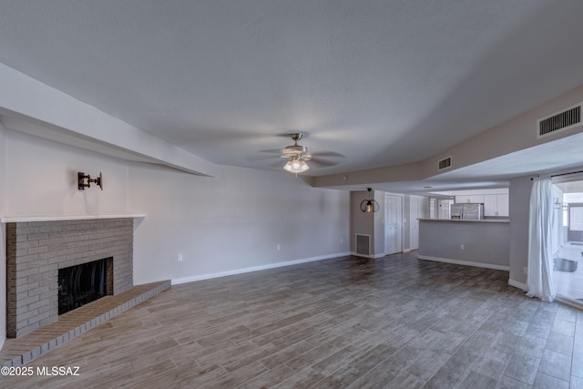 unfurnished living room with visible vents, a brick fireplace, light wood-style floors, and ceiling fan