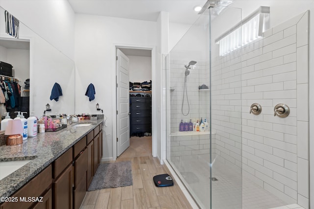 bathroom featuring double vanity, a walk in shower, wood finished floors, and a sink