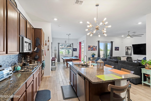 kitchen with light wood-type flooring, visible vents, a sink, stainless steel appliances, and decorative backsplash