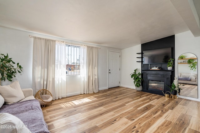 living room featuring light wood-type flooring, baseboards, a glass covered fireplace, and vaulted ceiling