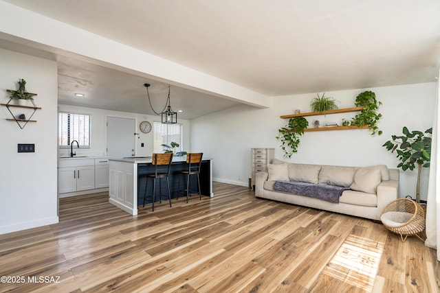 living area with beamed ceiling, baseboards, and light wood-style flooring