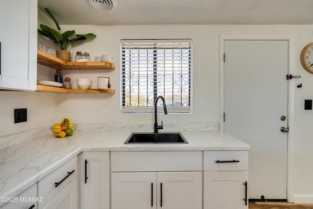 kitchen with visible vents, white cabinets, light stone countertops, and a sink