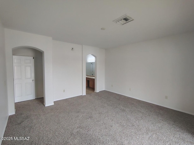 carpeted empty room with visible vents and arched walkways