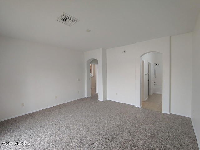 unfurnished room featuring arched walkways, visible vents, and light carpet