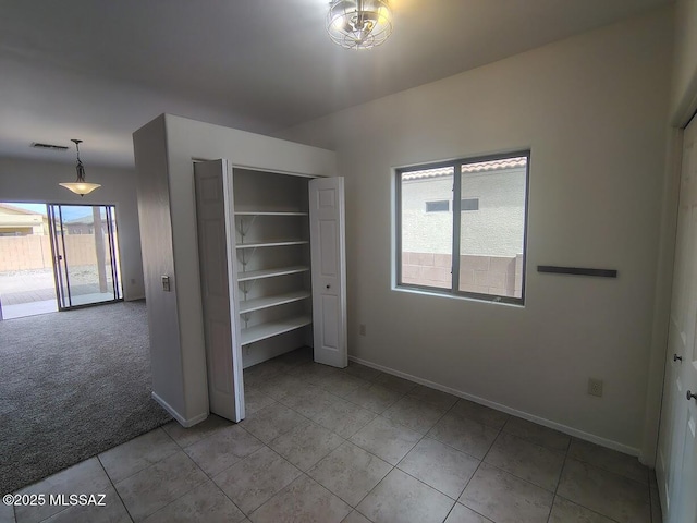 unfurnished bedroom with light tile patterned floors, visible vents, baseboards, a closet, and light colored carpet