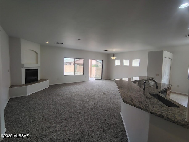 unfurnished living room featuring visible vents, baseboards, light colored carpet, and a fireplace with raised hearth