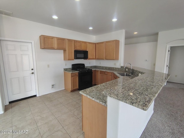 kitchen with light stone counters, a peninsula, a sink, black appliances, and brown cabinets